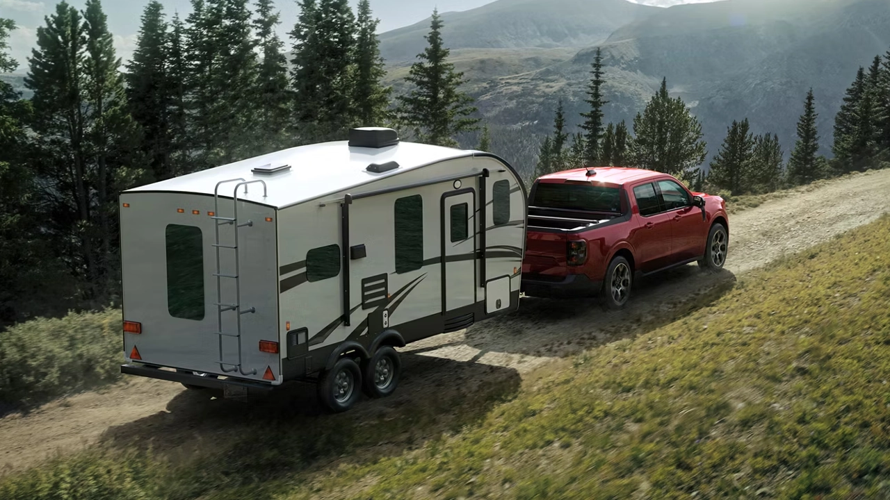 Ford Maverick 2026 rouge remorquant une grande roulotte blanche sur une route de campagne, mettant en valeur sa capacité de remorquage compacte