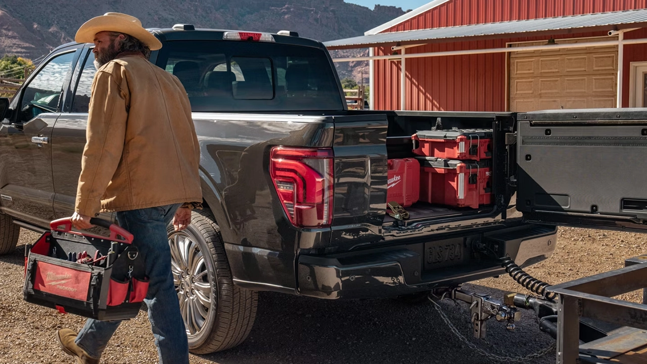 Travailleur chargeant des caisses à outils Milwaukee dans la boîte de pickup d'un Ford F-150 2026 noir, démontrant son espace de chargement utilitaire