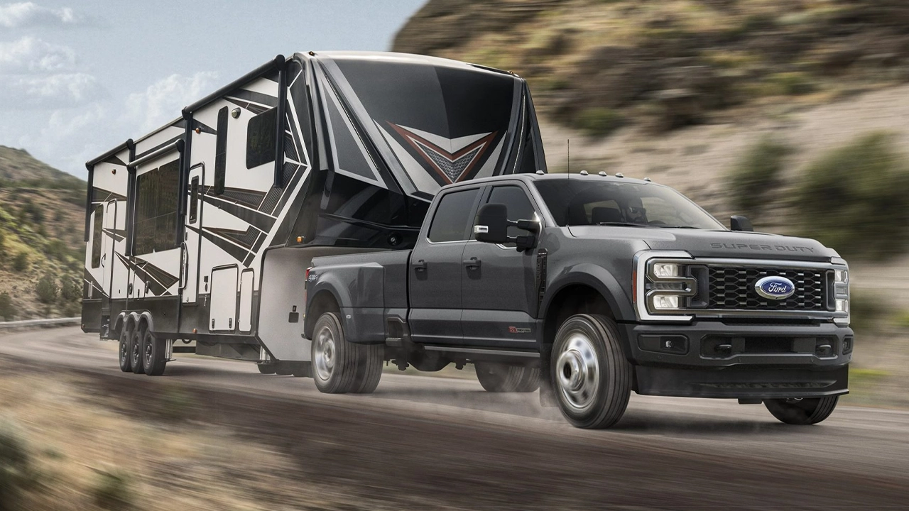 Ford Super Duty gris anthracite remorquant une grande caravane fifth-wheel sur une route de montagne.