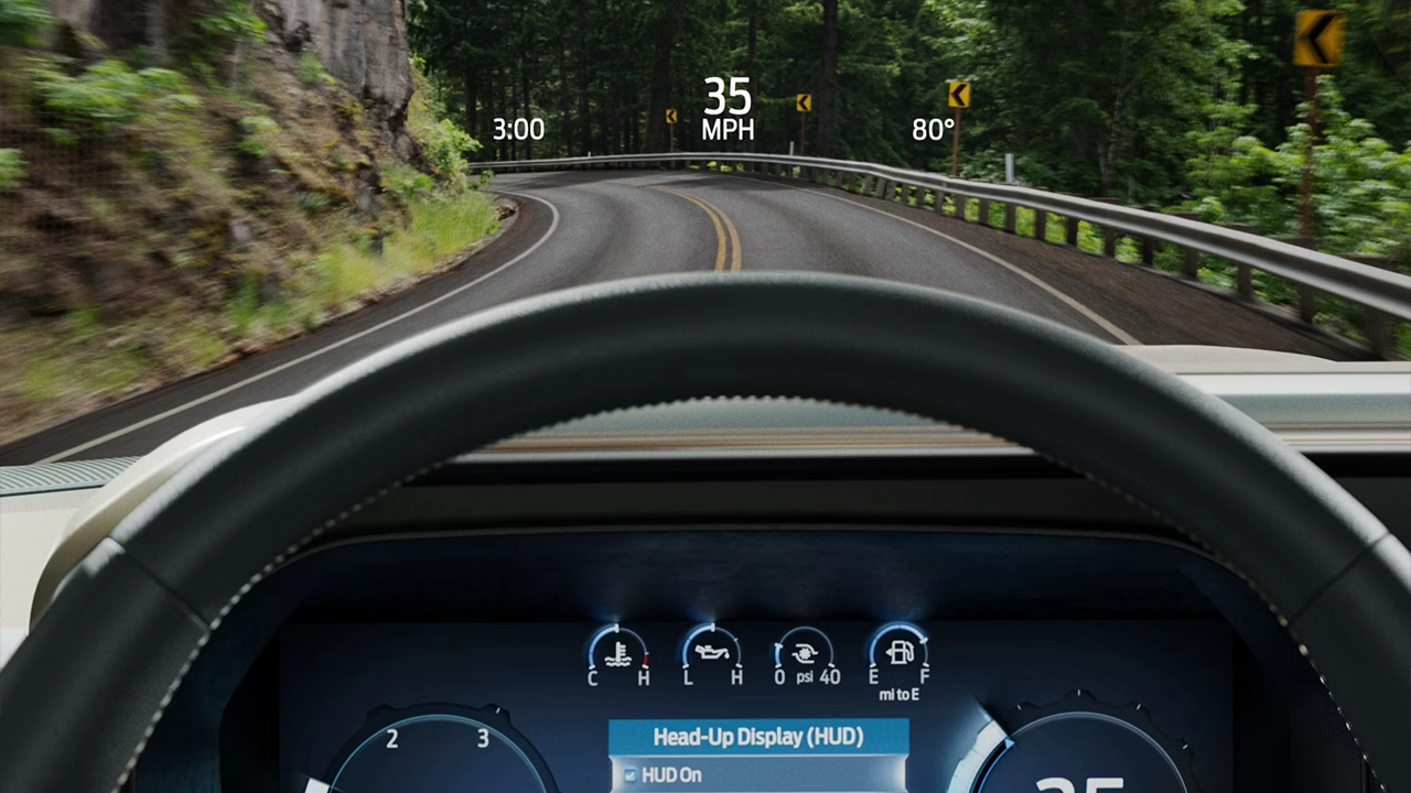 Vue conducteur du Head-Up Display (HUD) Ford affichant la vitesse (35 mph) et la température sur un pare-brise, en conduite sur une route forestière sinueuse.