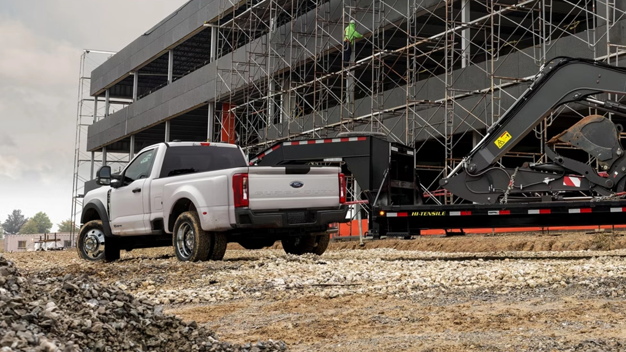 Ford Super Duty blanc cabine simple remorquant une remorque de chantier lourde sur un terrain de construction.