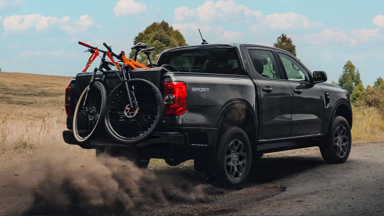 Ford Ranger Sport 2026 noir transportant des vélos sur chemin poussiéreux.