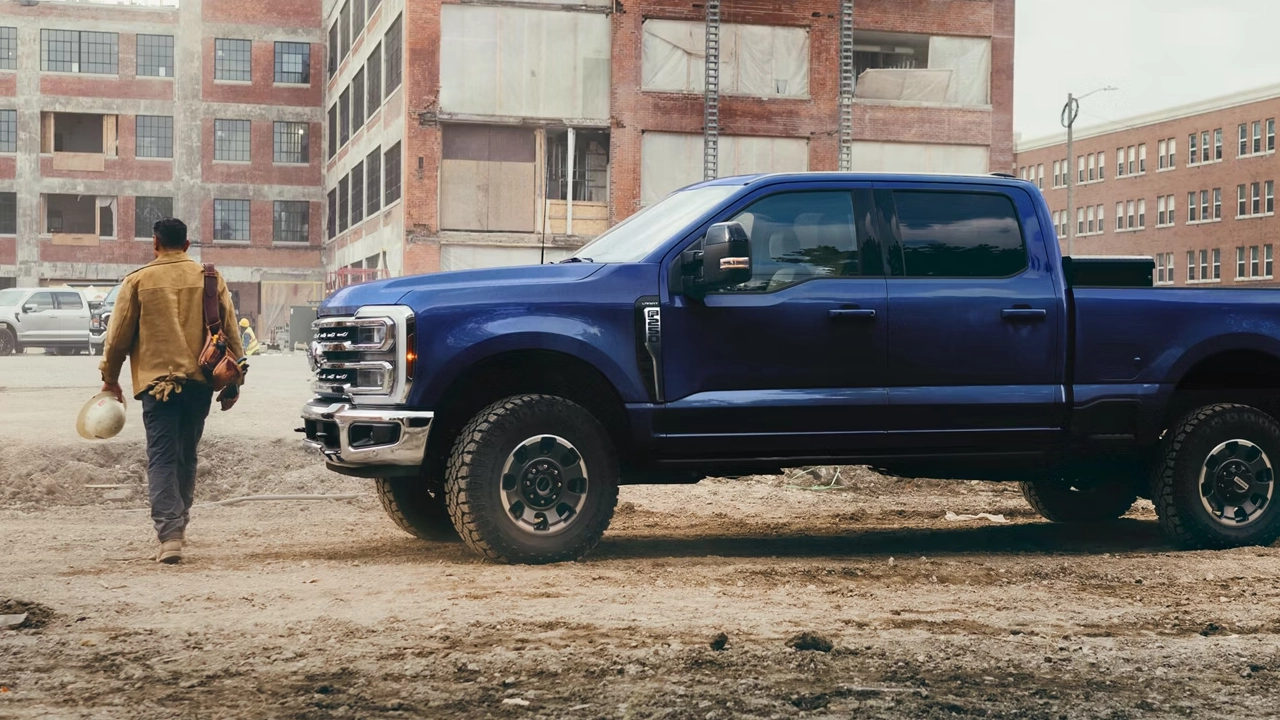 Ford F-250 Super Duty bleu foncé stationné sur un chantier urbain, avec un travailleur de la construction s'en approchant.