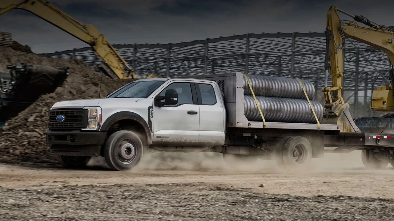 Ford F-550 Super Duty blanc transportant des tuyaux sur un chantier de construction