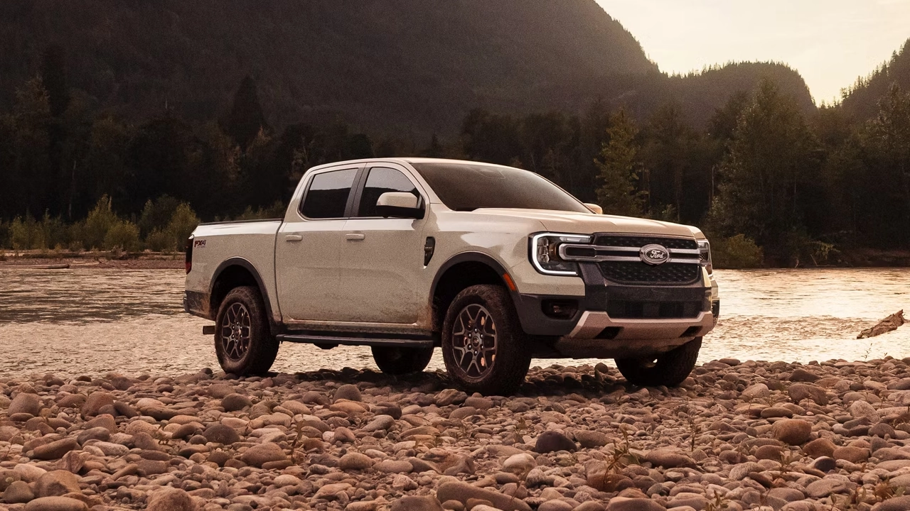 Ford Ranger blanc crème stationné sur un lit de rivière rocailleux, entouré de montagnes boisées au coucher du soleil.