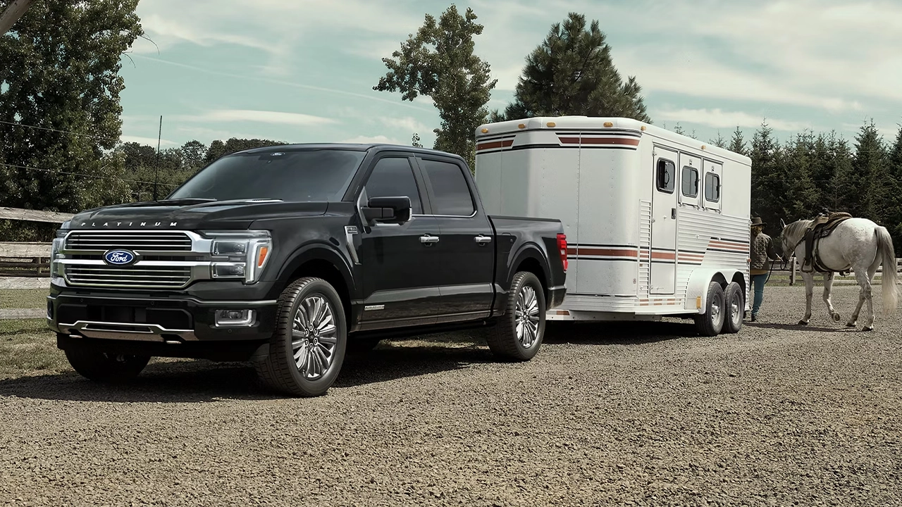 Ford F-150 Platinum noir remorquant une remorque à chevaux sur un ranch, avec un cavalier et son cheval blanc en arrière-plan.