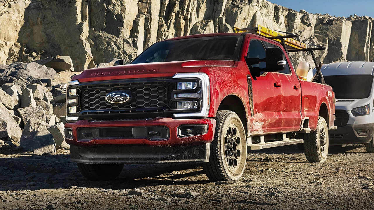 Ford Super Duty rouge couvert de boue avec une échelle sur le toit, stationné sur un chantier rocheux.