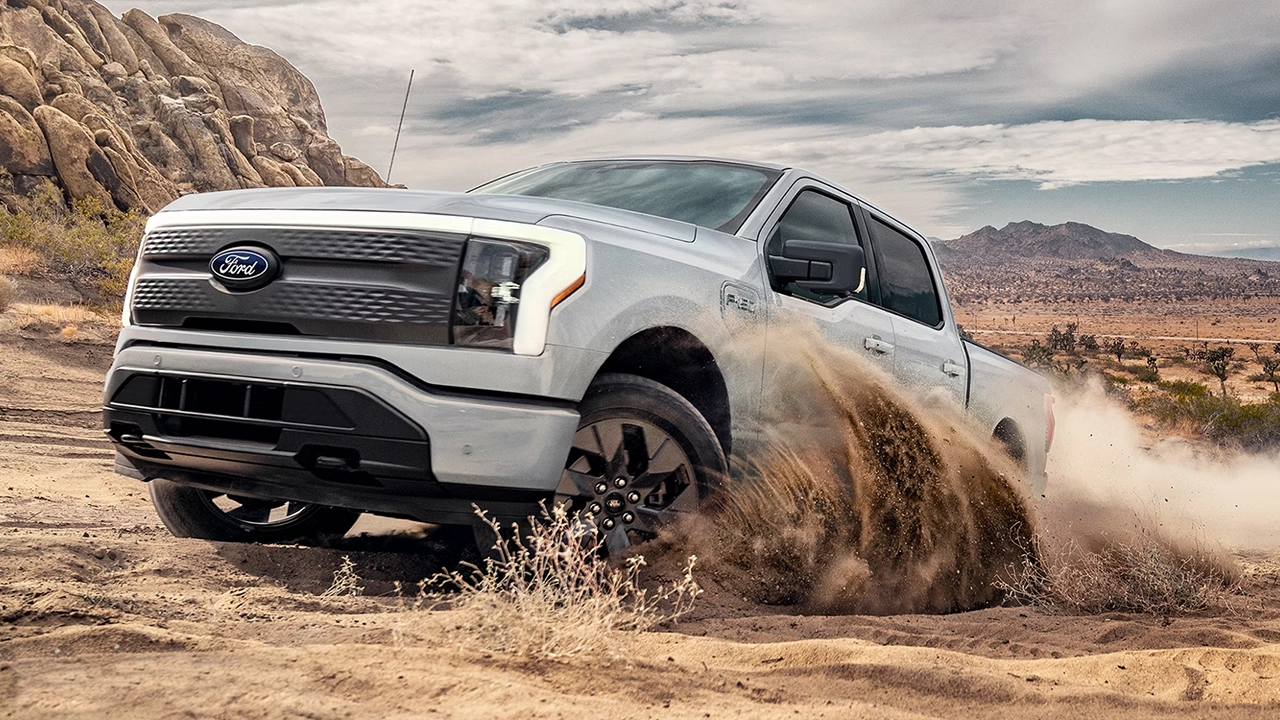 Ford F-150 Lightning blanc projetant du sable dans un virage en terrain désertique.