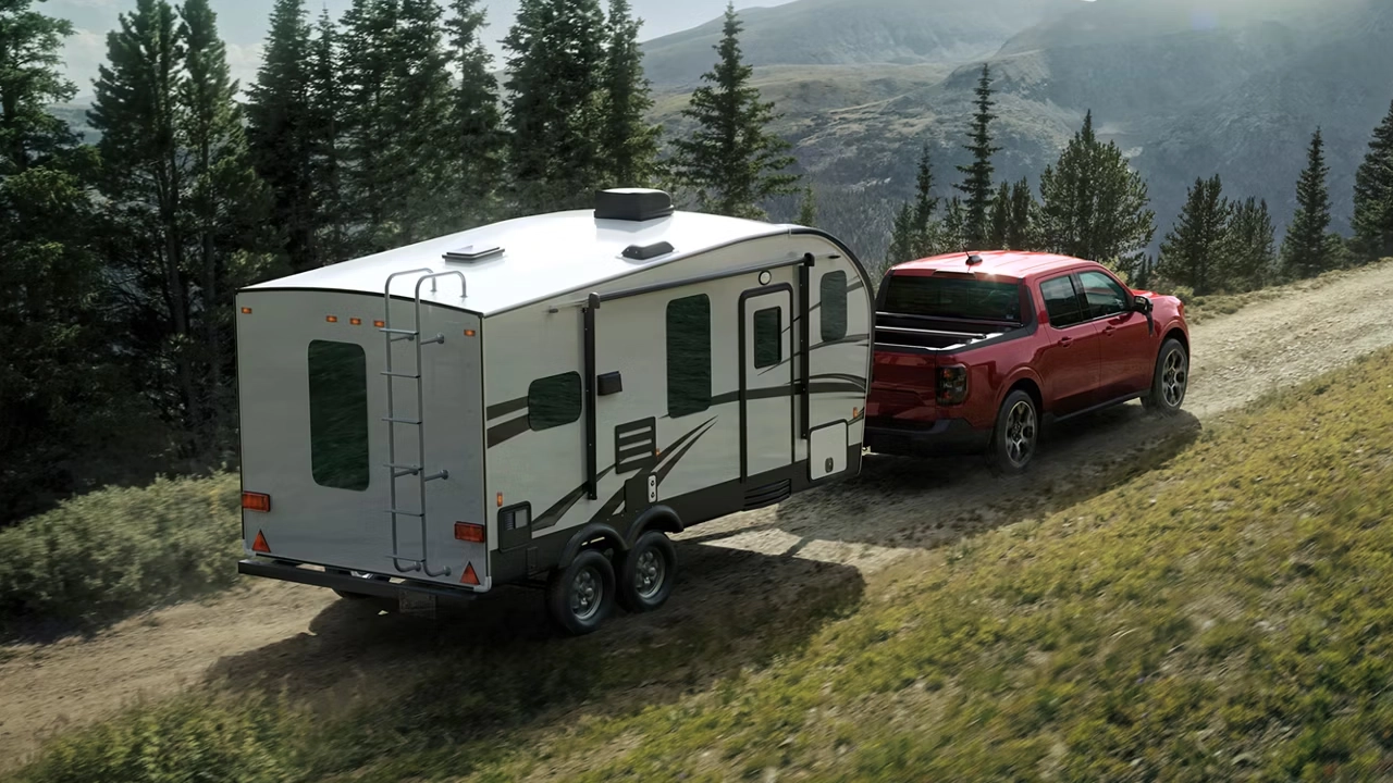 Ford Maverick rouge remorquant une caravane sur un chemin de montagne verdoyant.