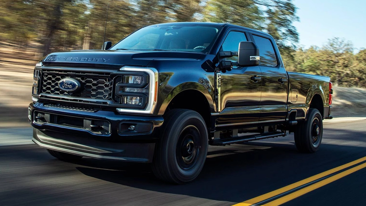 Ford Super Duty F-250 noir avec jantes noires en mouvement sur une route bordée d'arbres, vue de face trois quarts